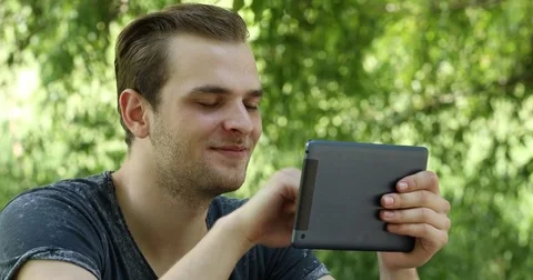 Happy Young Man Using a Digital Tablet Online Surfing Internet Outdoor Park Day Stock Footage 69724256