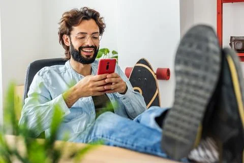 Happy young man using mobile phone relaxing at desk in the office Stock Photos