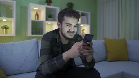 Happy young man using phone at home, pleasant and funny.  Stock Footage 234149936