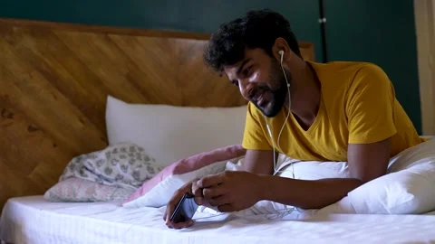 A happy young man using smart phone and earphones to chat with a wife,friends Видео 154732012