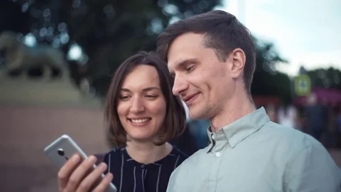 Happy young millennial couple using smartphone together in the park Stock Footage 79357594
