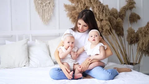 Happy young mom playing with two twin girls on the bed at home in cotton clothes Stock Footage 171571549
