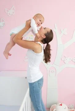 Happy young mother lifting cute baby out of crib Stock Photos