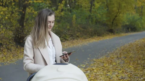 Happy, young mother using smartphone during a walk with baby in a pram in park Stock Footage 133207036