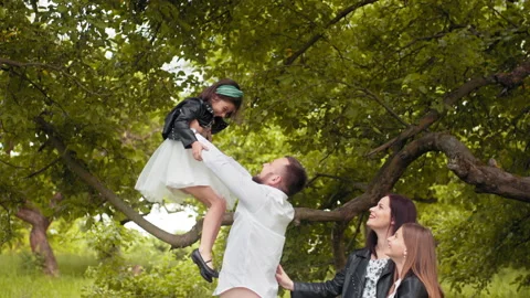 Happy young parents playing with cute little daughters at green garden Stock Footage 157651270
