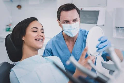 Happy young patient checking her teeth in clinic Stock Photos