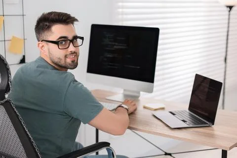 Happy young programmer working at desk in office Stock Photos