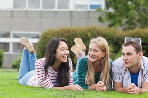 Happy young students lying on the grass on campus Photos