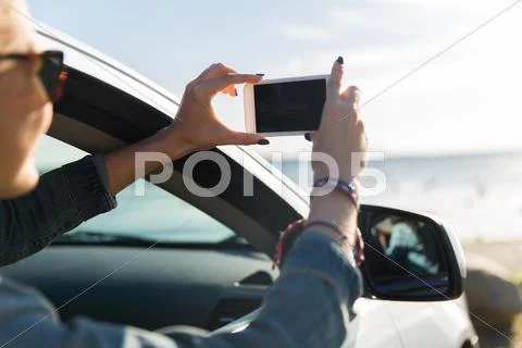 Happy young woman in car with smartphone at sea Stock Photos