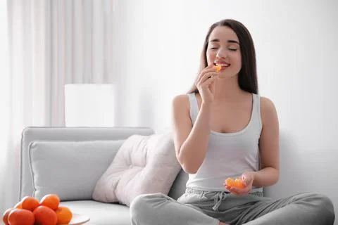 Happy young woman eating ripe tangerine at home Stock Photos