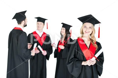 Happy young woman in mortarboard holding diploma and friends standing behind Stock Photos