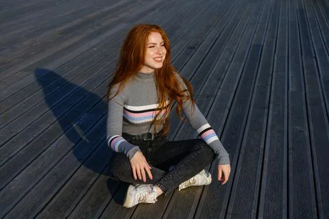 Happy young woman with red hair in the park on wooden flooring Stock Photos