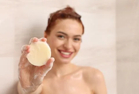 Happy young woman with solid shampoo bar in shower, selective focus. Space .. Stock Photos