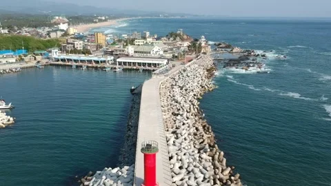 Harbor with rocks and a lighthouse distant beach in background in aerial view 動画素材 245199476