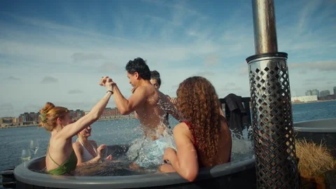 The harbor setting frames friends soaking in an outdoor hot tub spa Stock Footage 337880334