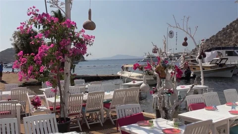 A harbor side restaurant with table and chairs, boats and jetty in background Stock Footage 82565249