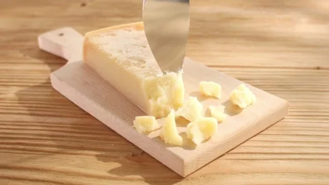 Hard cheese is chipped off with a knife on a cutting board. Wooden background. Stock Footage 244281393
