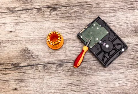 Hard disk and a red screwdriver with bits lays on wooden board. Stock Photos