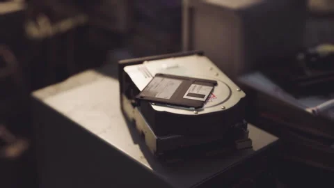 Hard drive and floppy disk placed on a dusty table in a cluttered workspace Stock Footage 312121263