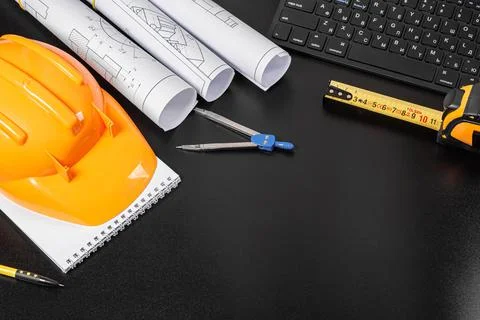 Hard hat, notepad, rolls of drawings on a black background with a keyboard an Stock Photos