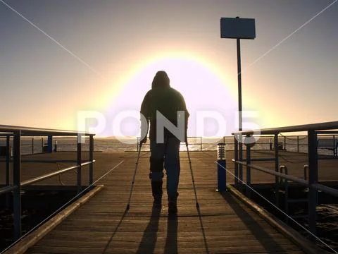 Hard walk of hurt man with crutches on port pier. Stock Photos