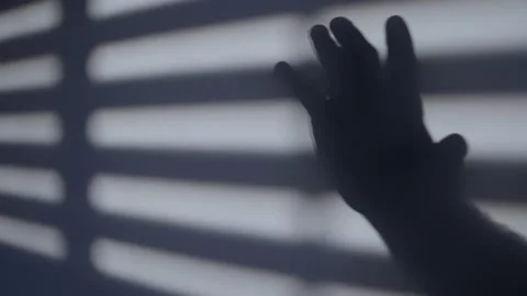 Hard window blind shadows cast on wall with hand shadow waving in dramatic scene Stock Footage 226231497