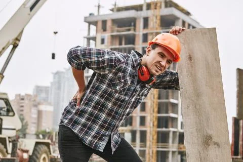 Hard work. Construction worker in protective helmet feeling back pain while Stock Photos
