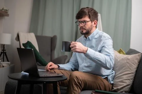 Hard work with the help of a young man's laptop, he sits on the couch, makes a Stock Photos