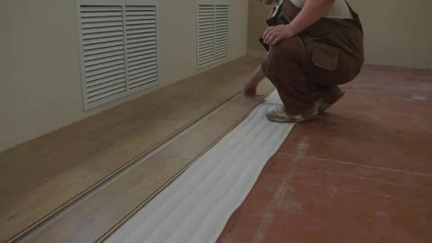 A hard-working construction worker in overalls carefully lays wooden laminate Stock Footage 326654972