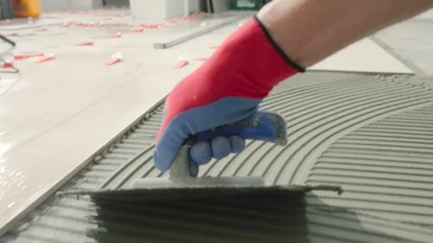 Hard working tiler spreading tile adhesive on the floor in preparation for Stock Footage 341134763