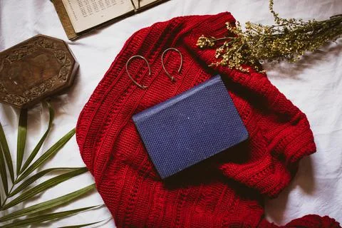 A hardcover diary with patterned blue binding on a red sweater with earrings  스톡 사진