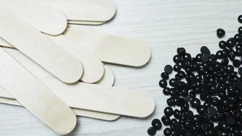 Hardened black wax pellets spread on rustic wooden surface with depilation Stock Footage 311975779