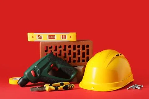 Hardhat with construction tools and brick on red background Stock Photos