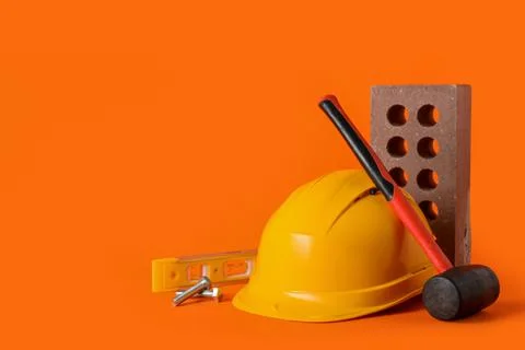 Hardhat with construction tools and brick on orange background Stock Photos