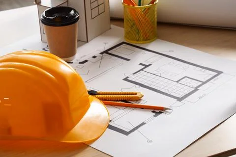 Hardhat with house plan and coffee cup on table in office, closeup Stock Photos