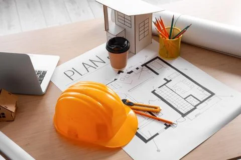 Hardhat with house plan and coffee cup on table in office Stock Photos