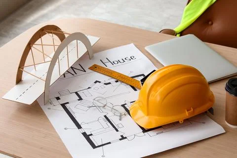 Hardhat with house plan, bridge model and laptop on desk in office Stock Photos