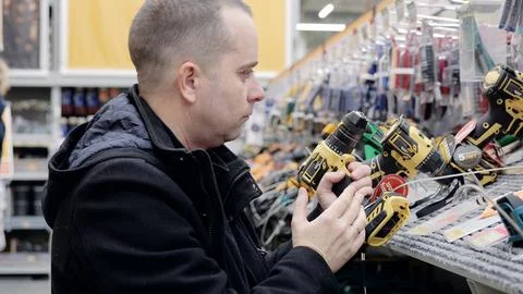 Hardware store customer comparing cordless screwdriver features, evaluating Stock Photos