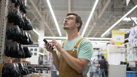 Hardware store worker in brown overalls, green shirt, checking inventory via Stock Footage 310903856