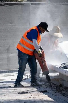 Hardworking construction laborer with jackhammer breaking concrete in dusty Stock Photos