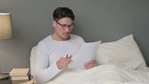 Hardworking Middle Aged Man Reading Documents in Bed Video stock 142367073