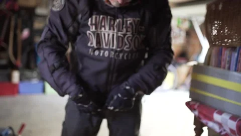 Harley Davidson biker puts on protection gloves and closes jacket in his Stock Footage 252575002