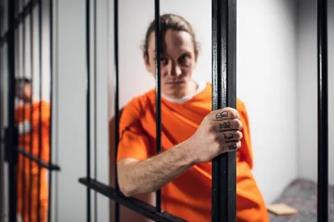 Harsh wild prisoner criminal maniac with tattoos grabs the bars. A close-up Stock Photos