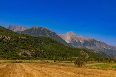 Harvested fields at the base of hills with mountains in the background under a Stock Photos