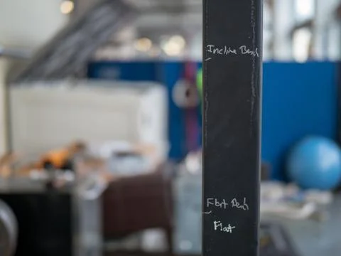 Hastily scribbled exercise markers on weight rack, makeshift gym in backgroun Stock Photos