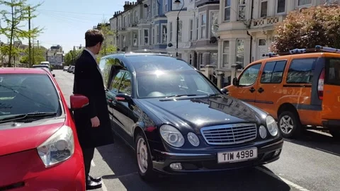 Hastings/UK 04-26-19 Funeral Director escorts hearse on foot to home of deceased Stock Footage