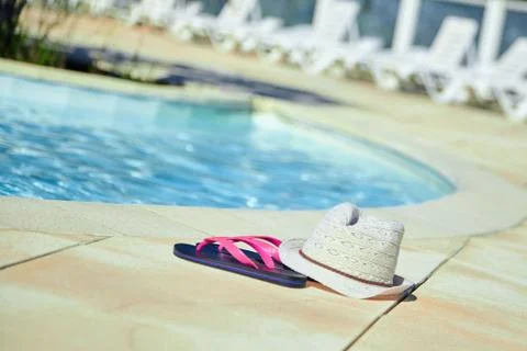 Hat and pink flip flops near the swimming pool with blue water, summer rest Stock Photos
