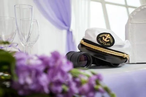 The hat of the captain on the table with binoculars and flowers Stock Photos