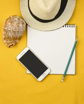 Hat on a yellow background with a notepad, phone, seashell and pencil. Stock Photos