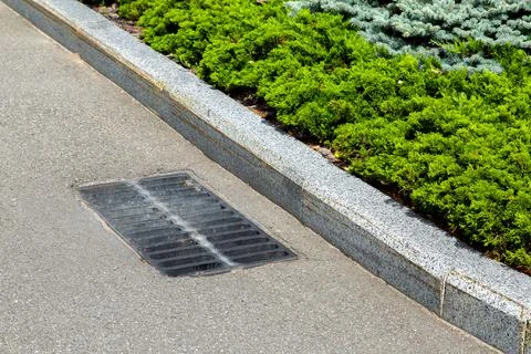 Hatch storm system with a grate in the asphalt road surface with stone curb. Stock Photos